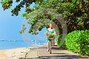 Young woman bicycling by waterfront road along tropical sea beach