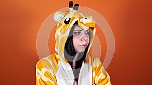 A young woman in a big pajamas of giraffe takes offence by something or someone on an orange background.