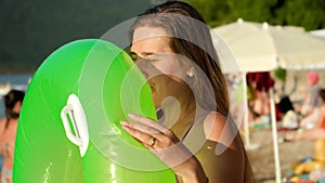 Young woman in bikini blowing air and inflating swimming ring on beach at summer holiday resort