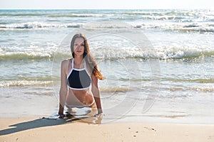 Young woman in bikini does Bhujangasana yoga asana or Cobra Pose on the sunny beach, front view.