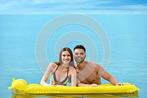 Young woman in bikini and her boyfriend with inflatable mattress in sea. Lovely couple