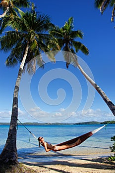Young woman in bikini laying in a hammock between palm trees, Of