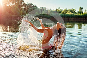 Young woman in bikini playing in river water and making splash. Girl having fun. Summer vacation activities