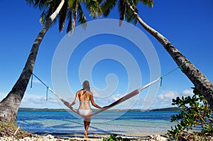 Young woman in bikini sitting in a hammock between palm trees, O