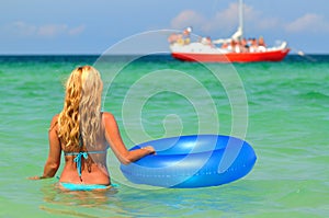 Young woman in bikini standing backwards in sea water with swimming circle