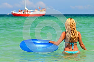 Young woman in bikini standing backwards in sea water with swimming circle