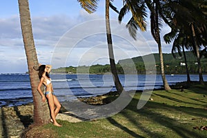 Young woman in bikini standing by palm tree, Las Galeras beach