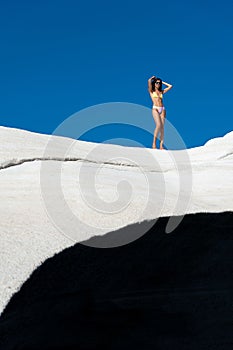 Young woman in a bikini standing on the rocky beach of Sarakiniko on the Greek island of Milos