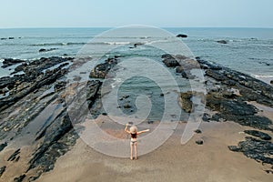 Young woman in a bikini and straw hat wawing on the sand near the waves of blue sea. Top view