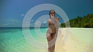 Young woman in bikini strolls along azure ocean water edge