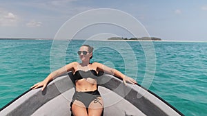 Young Woman in a Bikini and Sunglasses Lies on the Bow of Boat Floating by Ocean