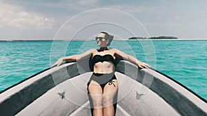 Young Woman in a Bikini and Sunglasses Lies on the Bow of Boat Floating by Ocean