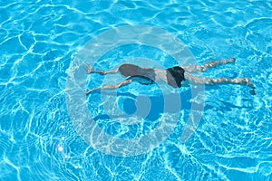 Young woman in bikini swimming underwater in an outdoor swimming pool, top view