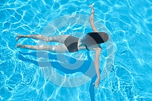 Young woman in bikini swimming underwater in an outdoor swimming pool, top view