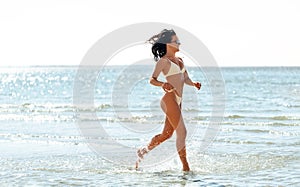 young woman in bikini swimsuit running on beach