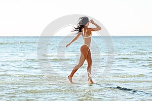 young woman in bikini swimsuit running on beach