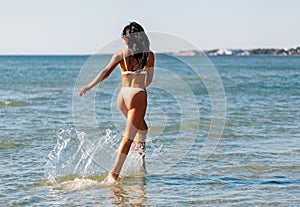 young woman in bikini swimsuit running on beach