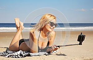 Young woman in bikini taking selfie photo with stick on the beac