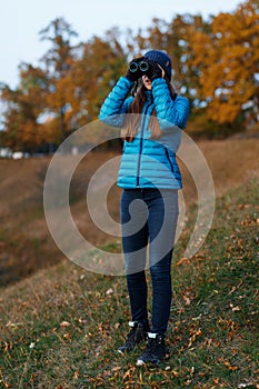 Young woman with binoculars watching birds in autumn park