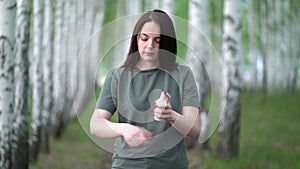 Young woman in a birch grove puts a mosquito repellent on her skin.