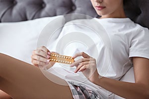 Young woman with birth control pills in bedroom