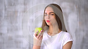 Young woman biting and eating tasty green apple. Healthy young woman eating green apple and smiling at home - indoors.