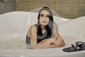 Young woman in a black bathing suit posing in the bath of milk