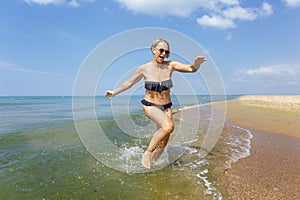 A young woman in a black bikini falls while running out of the sea on a sunny day. Activity and humor. Travel and holidays at the