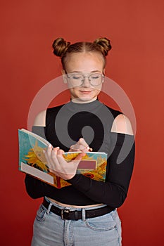 A young woman in a black blouse with a bun hairstyle writes in a notebook on a red background. university student
