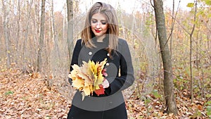 Young woman in the black coat holding a bouquet of autumn leaves