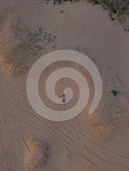 Young woman in a black dress lying on the back on the sand. Top view from the drone