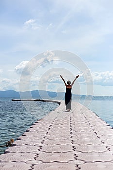 Young woman in black dress on pier in sea