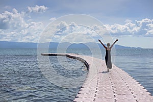 Young woman in black dress on pier in sea