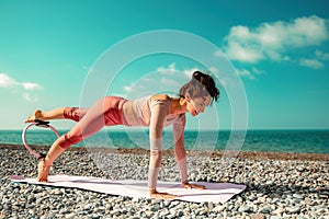 Young woman with black hair, fitness instructor in pink sports leggings and tops, doing pilates on yoga mat with magic