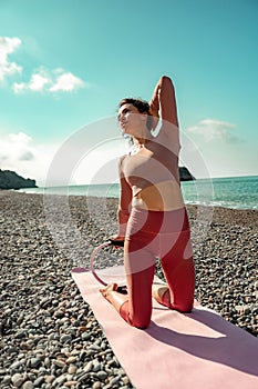 Young woman with black hair, fitness instructor in pink sports leggings and tops, doing pilates on yoga mat with magic