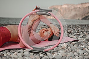 Young woman with black hair, fitness instructor in pink sports leggings and tops, doing pilates on yoga mat with magic