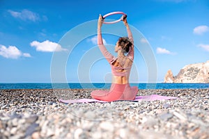 Young woman with black hair, fitness instructor in pink sports leggings and tops, doing pilates on yoga mat with magic