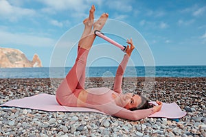 Young woman with black hair, fitness instructor in pink sports leggings and tops, doing pilates on yoga mat with magic