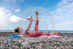 Young woman with black hair, fitness instructor in pink sports leggings and tops, doing pilates on yoga mat with magic