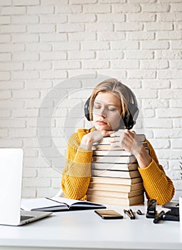 Young woman in black headphones listening to audio book with eyes closed sitting with a stack of books