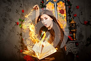 A young woman in a black mantle with a striped scarf around her neck casts a spell from a book and conjures with a wand of magic. photo