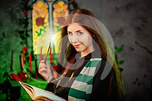 A young woman in a black mantle with a striped scarf around her neck casts a spell from a book and conjures with a wand of magic. photo