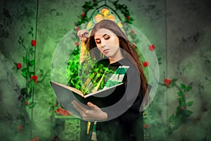 A young woman in a black mantle with a striped scarf around her neck casts a spell from a book and conjures with a wand of magic.