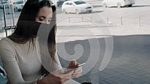 Young woman with black medical mask sending text message using smartphone