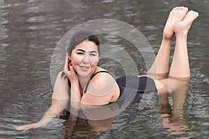 Young woman in black one-piece bathing swimsuit lying in outdoors pool at spa, hot springs resorts