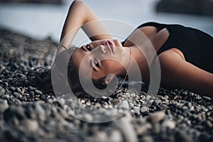 young woman in black skin-tight dress lying on the beach in water