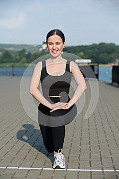 Young woman in black sportswear exercising outdoors. Fitness and healthy lifestyle concept.