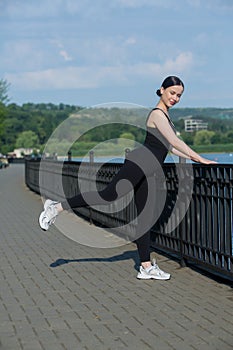 Young woman in black sportswear exercising outdoors. Fitness and healthy lifestyle concept.