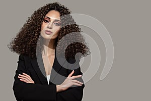 Young woman in black suit with crossed arms. female hairstyle afro curls. Beauty and fashion portrait