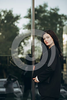 Young woman in a black suit looking to camera outside on street. Businesswoman portrait near office building.